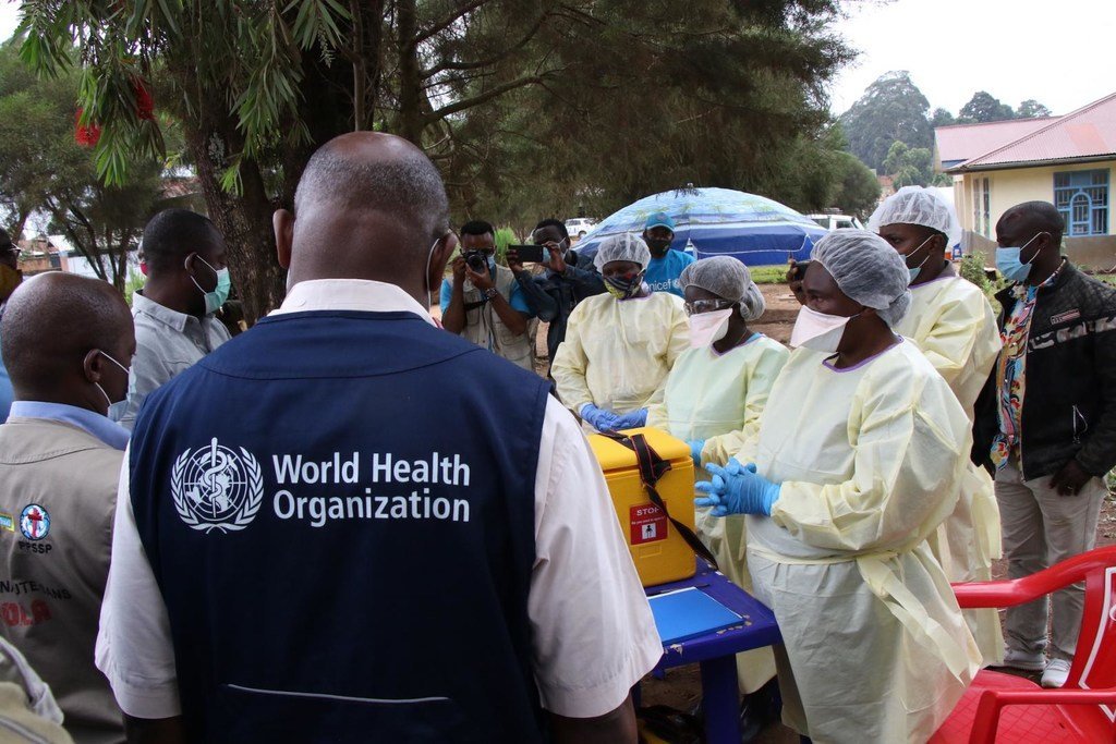 Kikundi cha wafanyakazi wa afya wa Shirika la Afya la Umoja wa Mataifa wakiwa wamevaa mavazi ya kinga wanasimama kando ya sanduku la biohazard la rangi ya manjano wakati wa jitihada za kukabiliana na Ebola nchini Guinea au Jamhuri ya Kidemokrasia ya Kongo.