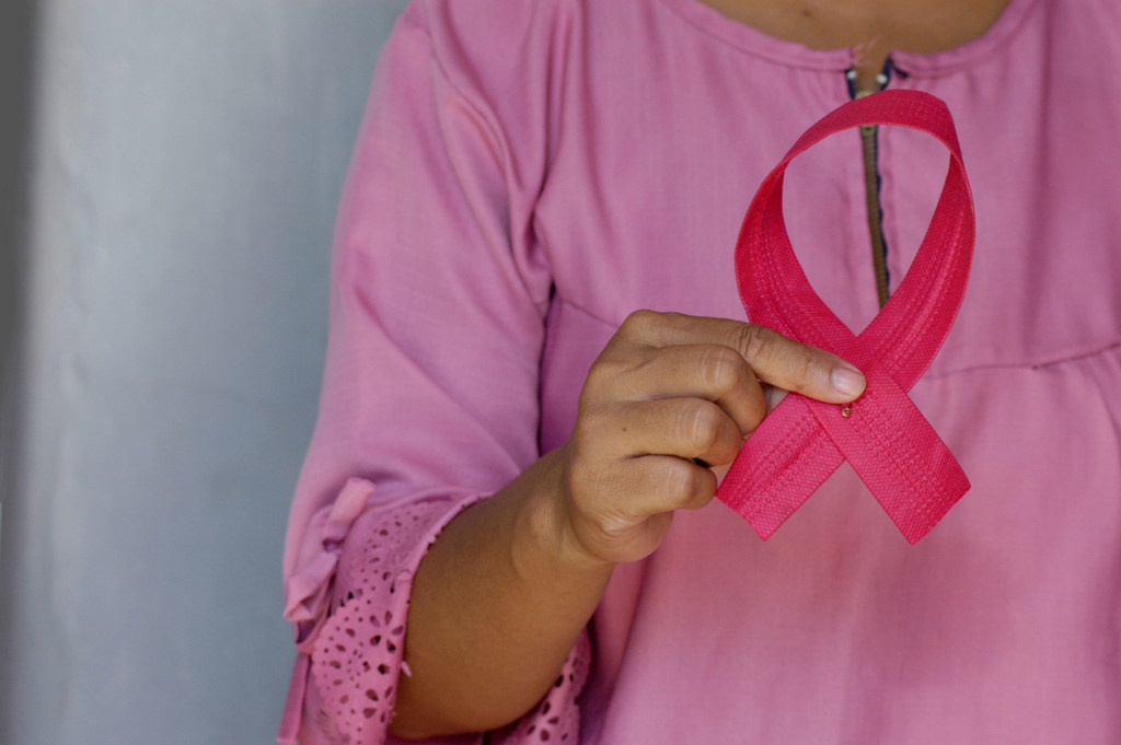 A woman holds a pink ribbon in awareness of Breast Cancer Day.