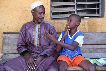 किसी देश में, एक बच्चा, जिसकी श्रवण क्षमता कमज़ोर है, वो अपने पिता को संकेत भाषा सिखाते हुए.