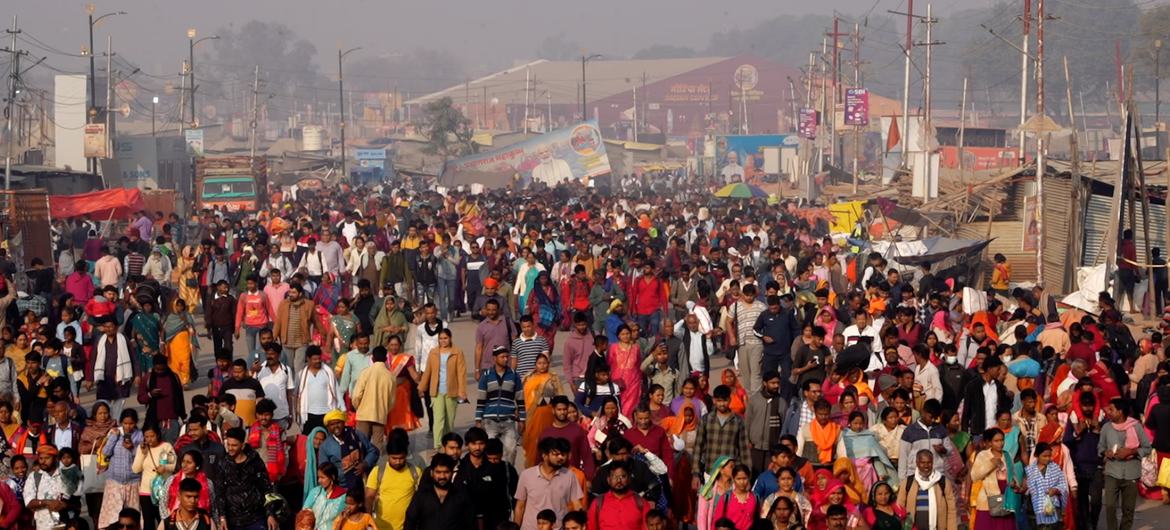भारत में महाकुंभ मेले के दौरान विभिन्न पृष्ठभूमियों के लोगों की एक विशाल भीड़ धूल भरी सड़क पर चल रही है।