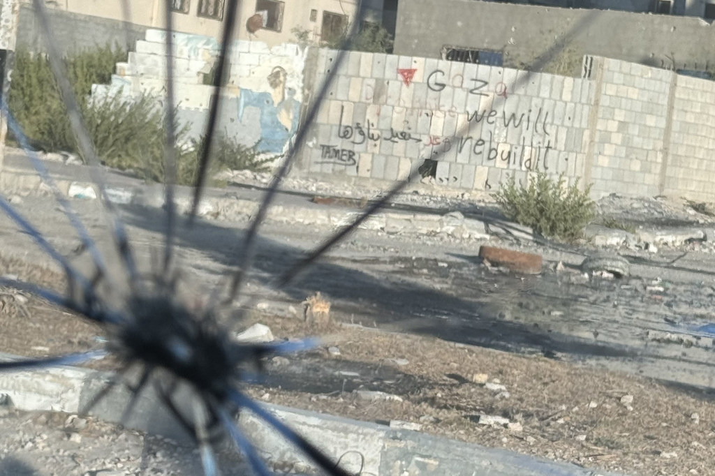 Un grafiti en un muro de hormigón en la ciudad de Gaza muestra el mensaje "Gaza, la reconstruiremos" a través de una ventana rota.