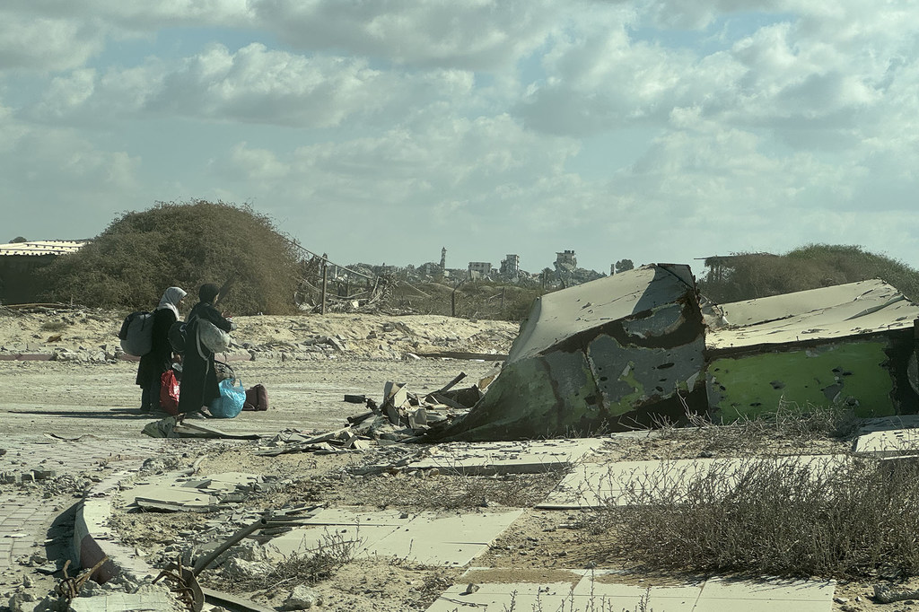 Dos mujeres palestinas con bolsas y pertenencias caminan por un paisaje de escombros y edificios destruidos en el norte de Gaza.