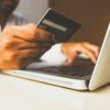 Uma pessoa utiliza um cartão de crédito para fazer uma compra online em um laptop.