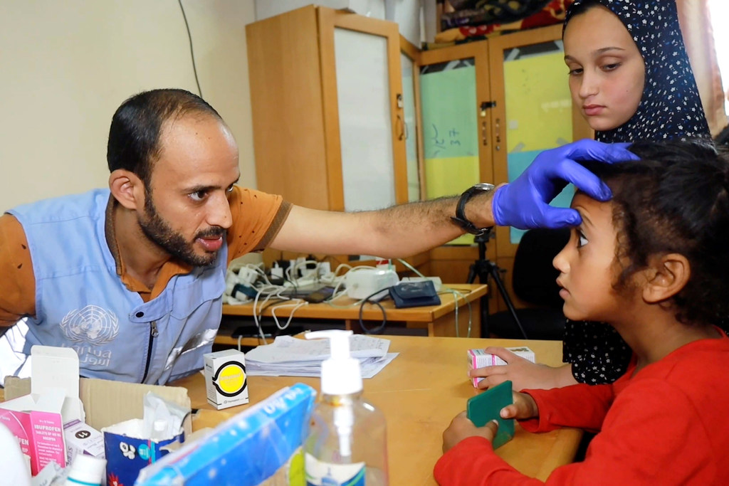عبد الرحمن أبو عمرة، ممرض يعمل في عيادة مدرسة ذكور دير البلح الإعدادية في دير البلح والتي تحولت إلى مركز للنزوح، يقوم بفحص الأطفال في العيادة.