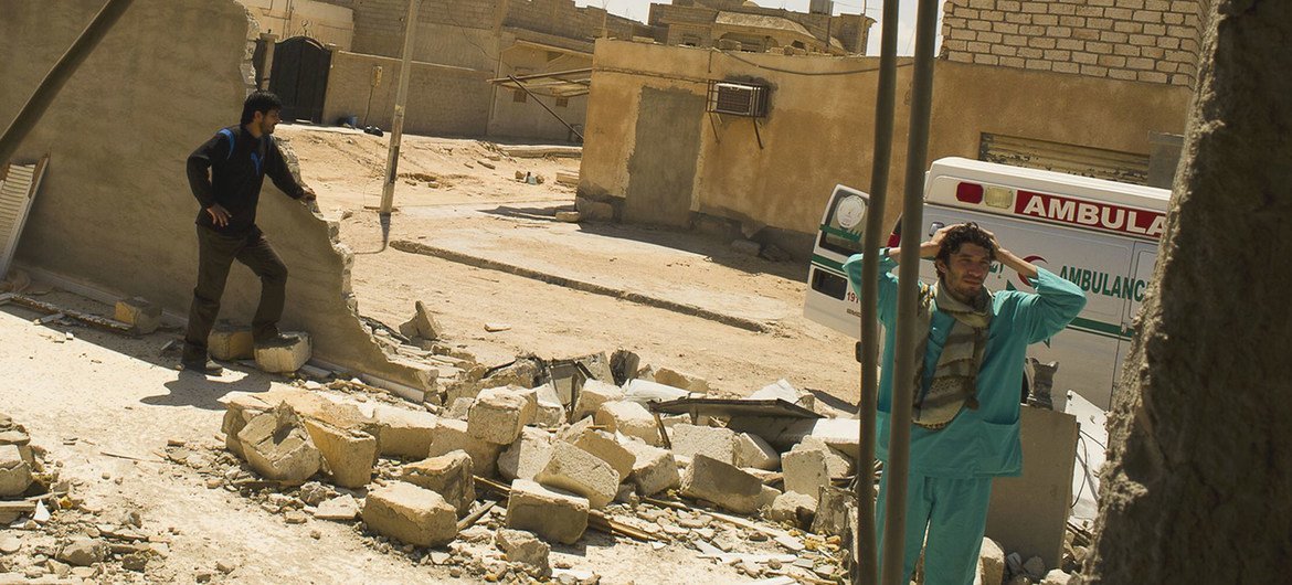 رجلان في مبنى مدمر في أجدابيا، ليبيا. يقف أحدهما وسط الأنقاض، بينما يقف الآخر بجوار سيارة إسعاف متضررة.