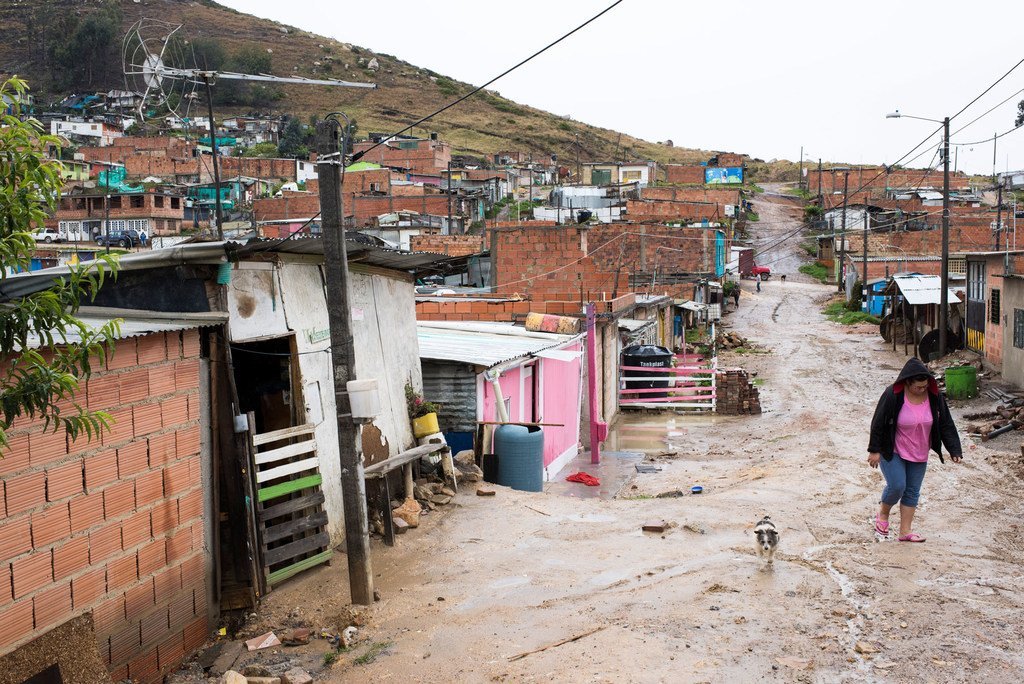 Una mujer pasea con su perro por un camino de tierra embarrado en un asentamiento informal en la ladera de una colina en Bogotá, Colombia.