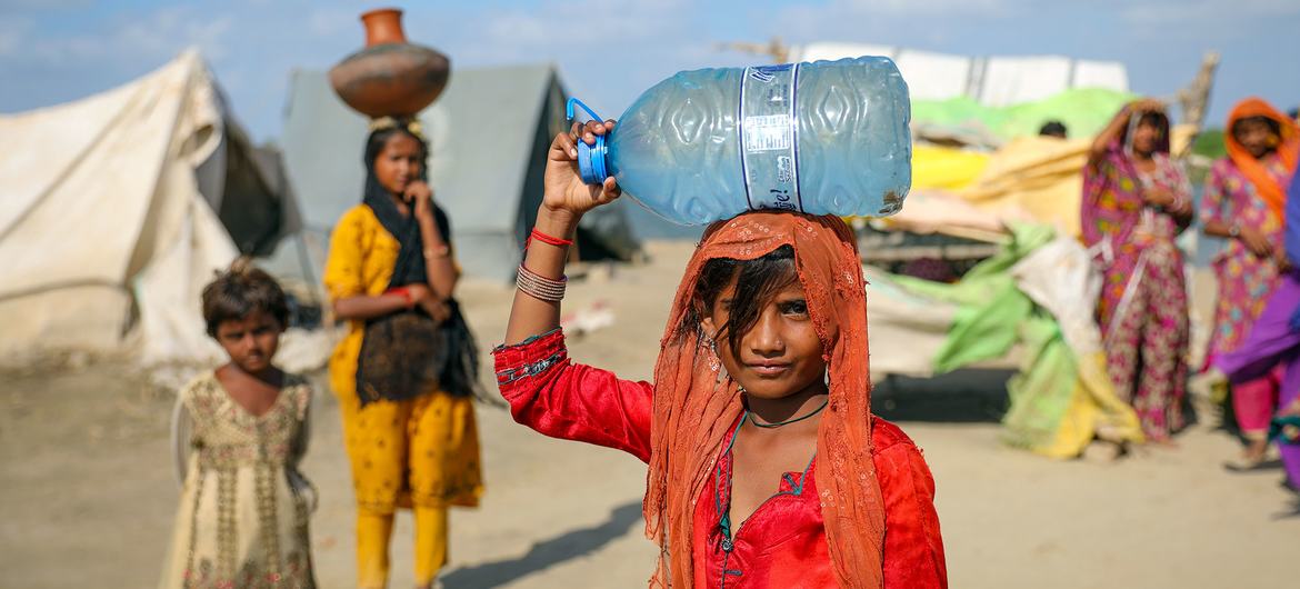 Uma menina de nove anos carrega água, que ela encheu de uma bomba manual em uma vila inundada na província de Sindh, no Paquistão.