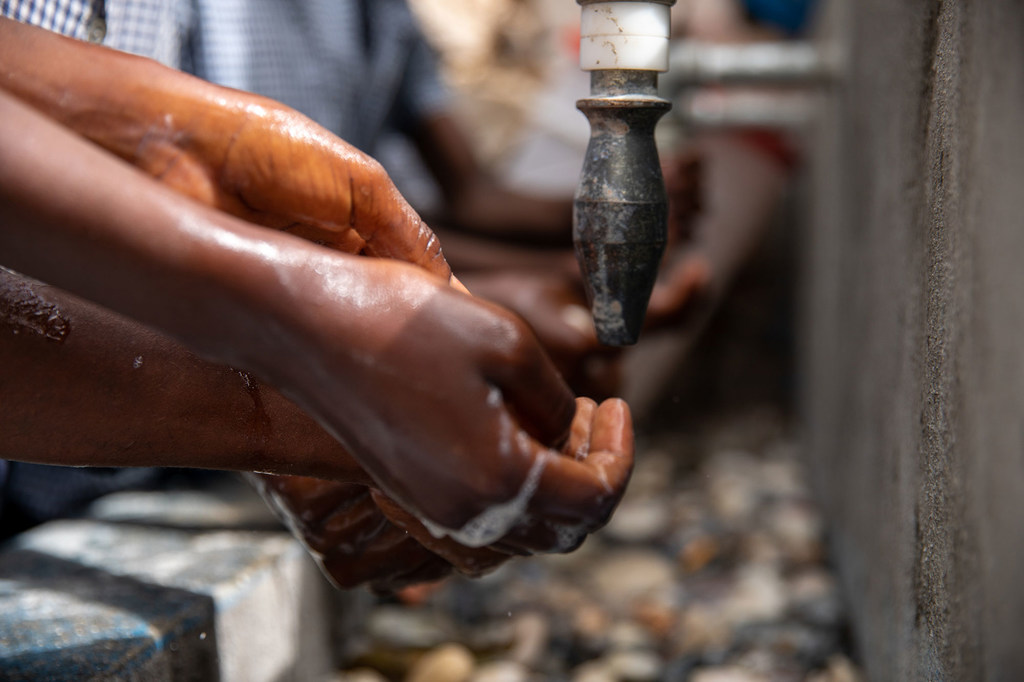Primer plano de unas manos siendo lavándose con jabón bajo un grifo en un punto de agua en Haití.
