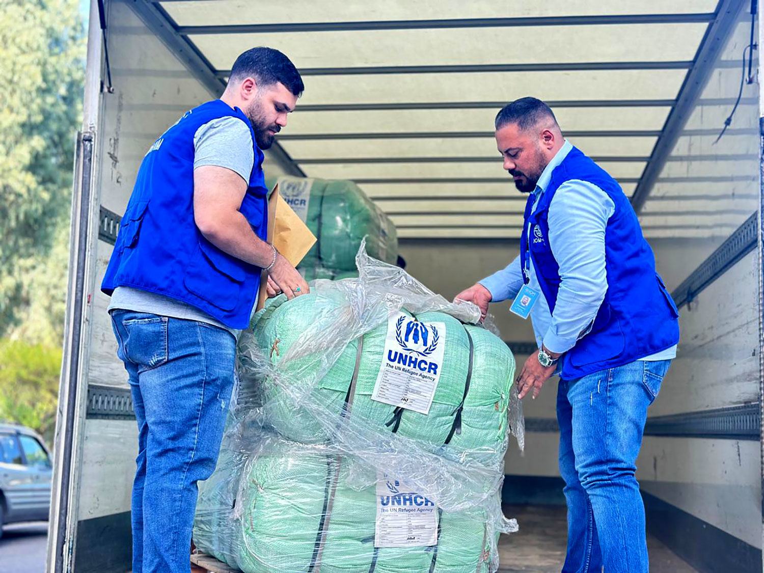 Deux hommes en gilets bleus chargent des fournitures d'aide du HCR dans un camion au Liban.