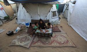 Una mujer sentada con sus tres hijos en un campo de desplazados del oeste de Gaza; su bebé sólo tiene dos meses.