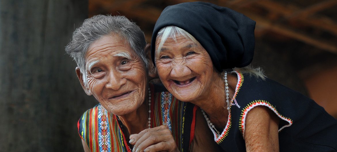 Two elderly Vietnamese women in traditional attire share a joyful moment, symbolizing community resilience and hope during the UN75 anniversary celebrations.
