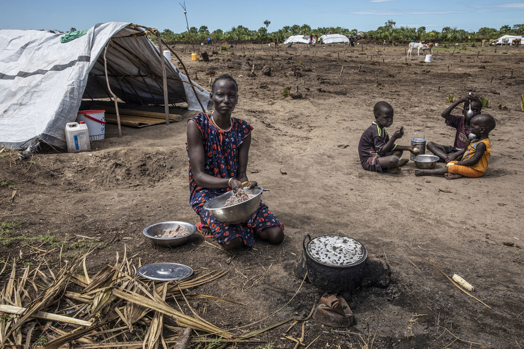Nyabin Bang prepara comida en un cuenco de metal en el campamento ganadero de Ding Ding, en el estado de Unity, Sudán del Sur, mientras los niños comen cerca.