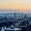 Vista do horizonte de Viena ao entardecer, com a torre Volksgartentor, a prefeitura iluminada e outras torres e cúpulas históricas contra um céu alaranjado suave.