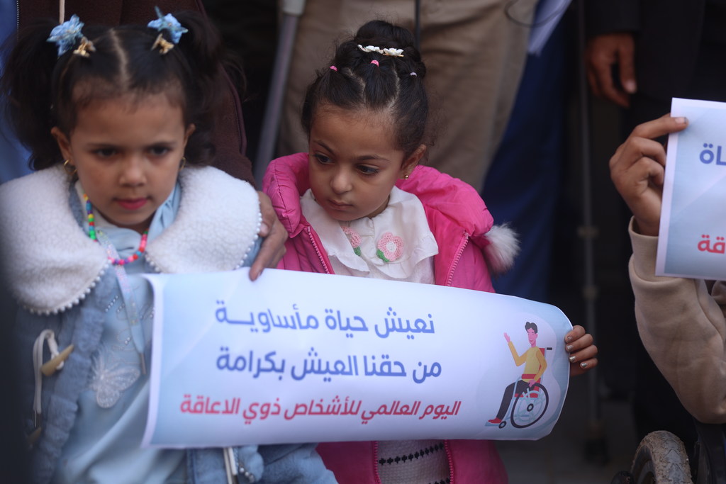 فتاتان فلسطينيتان صغيرتان في غزة تحملان لافتة باللغة العربية خلال فعالية بمناسبة اليوم العالمي للأشخاص ذوي الإعاقة.