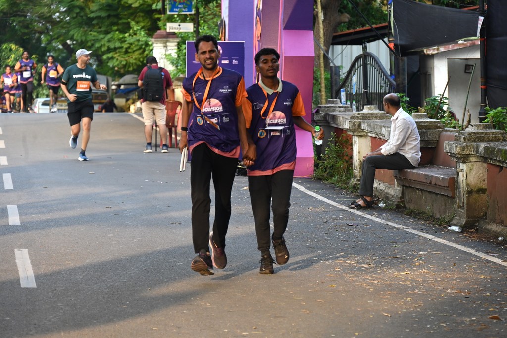 UN इंडिया पर्पल फेस्ट 2025 मैराथन में दो भारतीय पुरुष, जिनमें से एक कृत्रिम पैर का इस्तेमाल कर रहा है, पदक पहने हुए हाथ में हाथ डालकर चल रहे हैं।