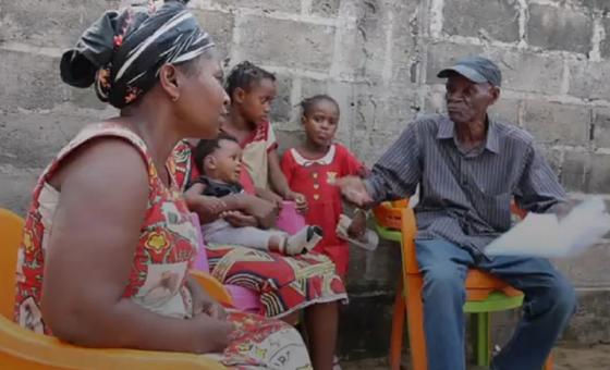 Veronique Loukombo, mkazi wa Biloungou, Kongo, ameketi na watoto wake huku akizungumza na mwanamume mbele ya ukuta wa mawe.