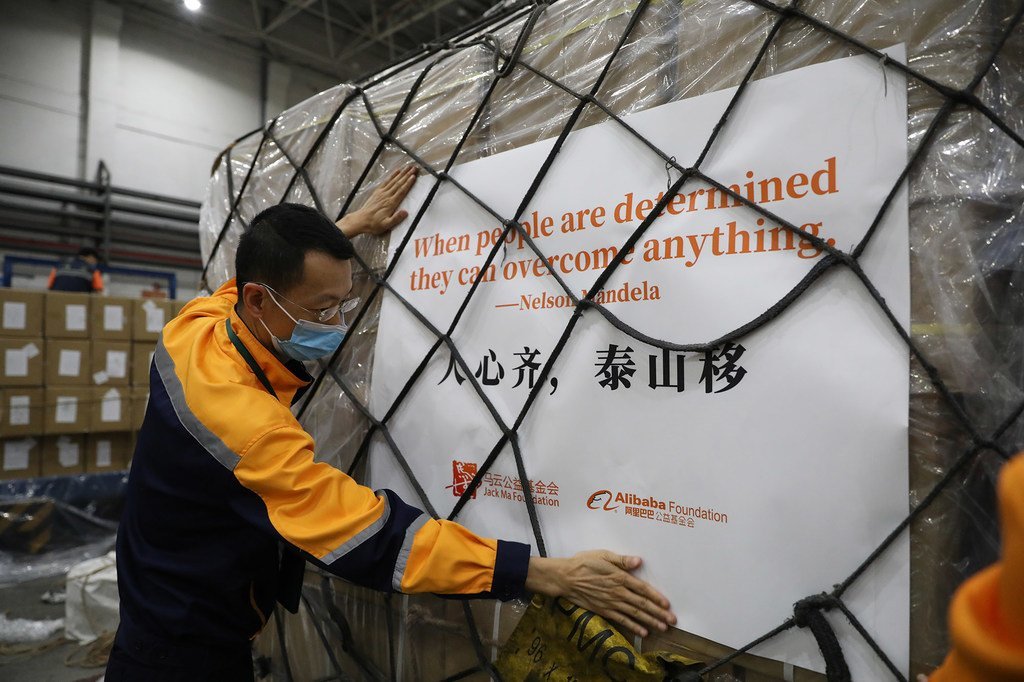 一名戴着口罩的男子正在搬运一托盘运往非洲的人道主义援助物资。这些物资包装上印有纳尔逊·曼德拉的名言以及马云公益基金会和阿里巴巴公益基金会的标志。