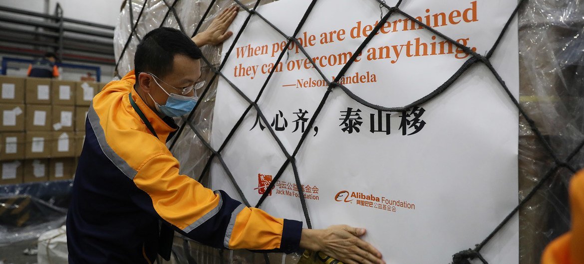 一名戴着口罩的男子正在搬运一托盘运往非洲的人道主义援助物资。这些物资包装上印有纳尔逊·曼德拉的名言以及马云公益基金会和阿里巴巴公益基金会的标志。