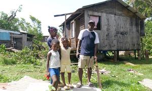 A family stands outside their home damaged by Hurricane Beryl in St. Andrews, Grenada.