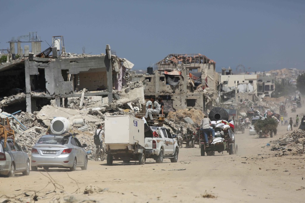Mtaa mmoja huko Gaza unaonyesha majengo na vifusi vilivyoharibiwa, huku watu na magari wakipitia kwenye vifusi.