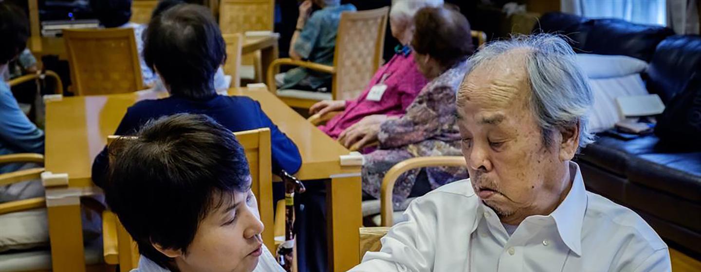 Una cuidadora examina el brazo de un anciano asiático en lo que parece ser un centro de atención.
