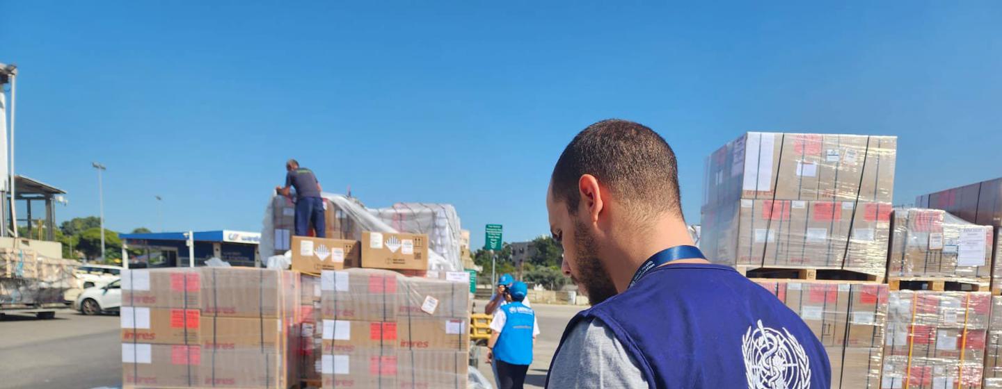 Un employé de l'OMS examine un bloc-notes dans un port de Beyrouth, entouré de piles de fournitures médicales arrivant au Liban.
