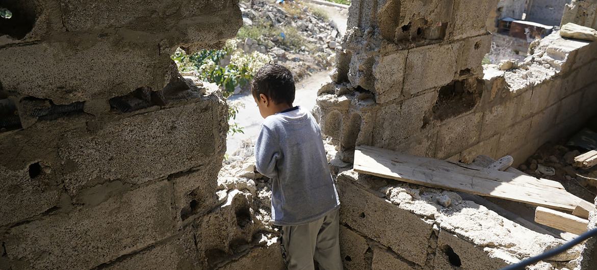 यमन के एक युद्ध प्रभावित इलाक़े में, एक बच्चा अपने क्षतिग्रस्त घर से बाहर की तरफ़ देखता हुआ.