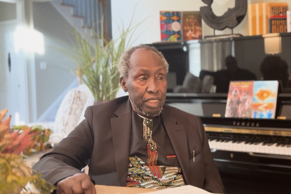Ngũgĩ wa Thiong'o, profesa kutoka Chuo Kikuu cha California, Irvine, ameketi katika mazingira ya ndani huku piano ikiwa nyuma.