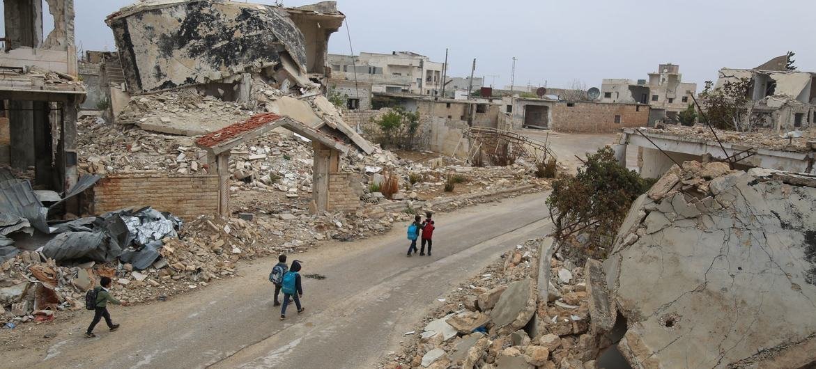 Sur le chemin du retour de l'école, des enfants marchent devant des ruines en Syrie.