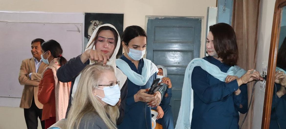 ایک بیوٹیشن سیلون میں ایک کلائنٹ کے بالوں کو اسٹائل کر رہی ہے، جس میں دیگر خواتین پس منظر میں دیکھ رہی ہیں۔ یہ منظر ملتان، پاکستان میں ترتیب دیا گیا ہے۔