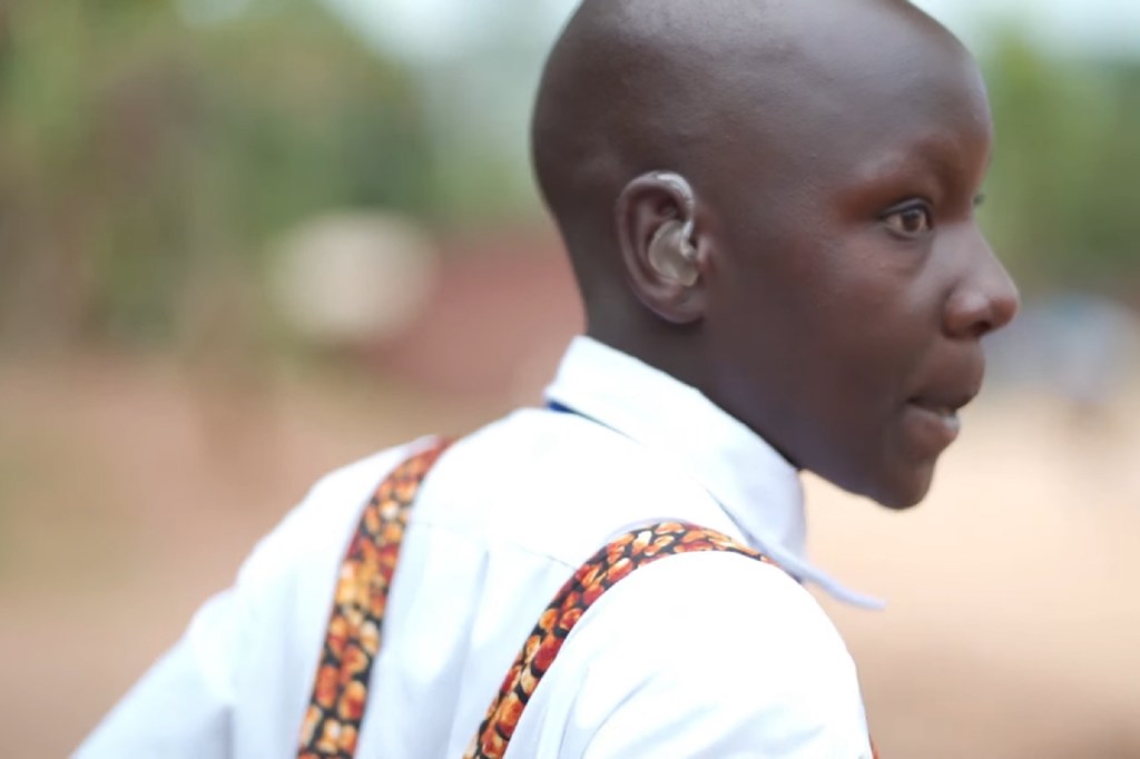 Pascaline Uwamayeyi, mwanafunzi wa shule ya msingi nchini Rwanda, akiwa amevaa kifaa cha kusaidia kusikia na shati jeupe lenye vishikio vya kushikilia.