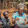 Wanawake wanne huko Kivu Kusini, DRC, wanashiriki katika mpango wa FAO . Mwanamke mmoja katikati akipitia vifaa vya kielimu huku wengine wakiangalia wakiwa nje.