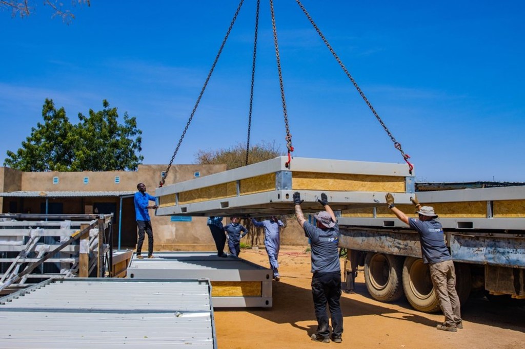 Wafanyakazi katika kituo cha Farchana IOM huko Chad wakishusha paneli kubwa ya chuma kutoka kwa lori kama sehemu ya mradi wa upanuzi wa kukabiliana na migogoro ya Sudan.