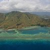 Vista aérea de uma costa tropical com montanhas verdes, uma praia de areia e águas turquesa com um recife de coral perto de Dili, Timor-Leste.
