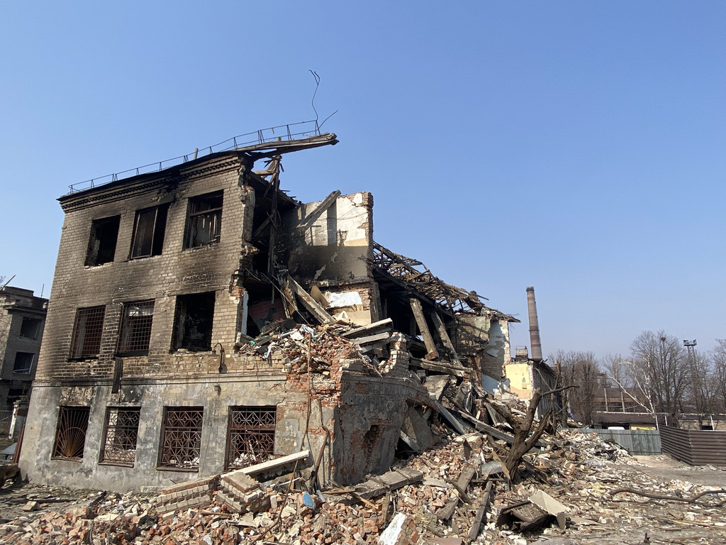 A severely damaged, multi-story building in Dnipro, Ukraine, with a large section of its structure collapsed into rubble under a clear blue sky.