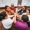 Um grupo de mulheres em uma área rural da Colômbia está reunido em círculo, de mãos dadas e com sorrisos no rosto.