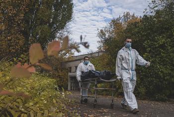 Duas enfermeiras com trajes de proteção contra materiais perigosos e máscaras faciais empurram uma maca com um saco para cadáveres ao longo de um caminho em um hospital em Kharkiv, na Ucrânia, durante a pandemia de COVID-19.