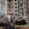 A woman walks past destroyed apartment buildings and vehicles in Chernihiv, Ukraine.