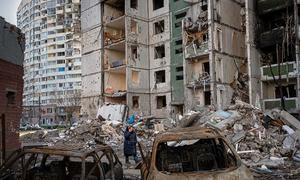 A woman walks past destroyed apartment buildings and vehicles in Chernihiv, Ukraine.