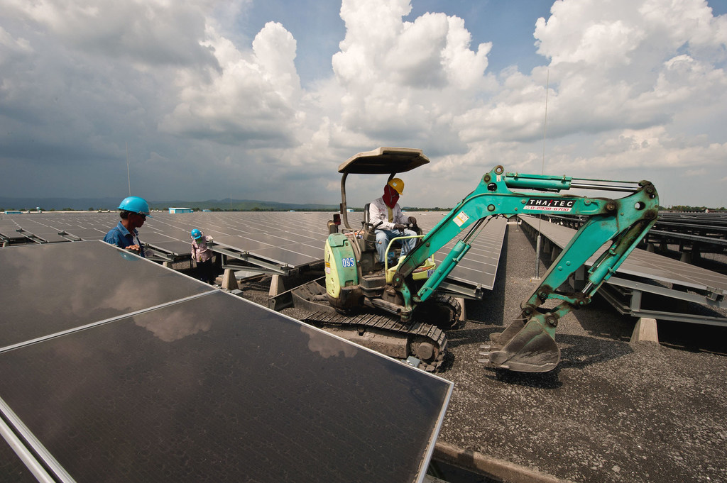 Trabajadores instalando paneles solares en la planta de energía solar de Lopburi en Tailandia, con una pequeña excavadora en el lugar.