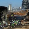 Un pompier libanais arrose les débris sur le site de l'explosion du port de Beyrouth, avec des bâtiments endommagés en arrière-plan.