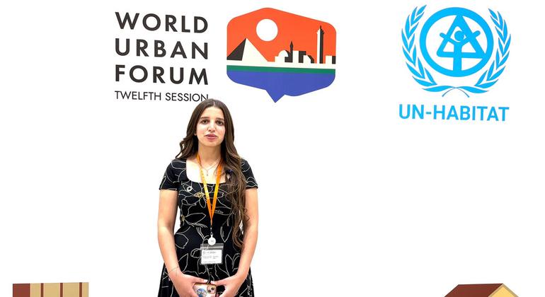A woman stands at a press conference for the World Urban Forum's Twelfth Session, with UN-Habitat logos displayed behind her.