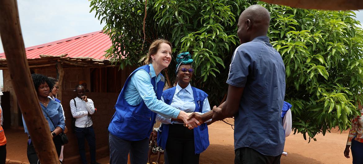Amy Pope aperta a mão de um homem em Moçambique, com outra mulher vestindo um colete da OIM entre eles.