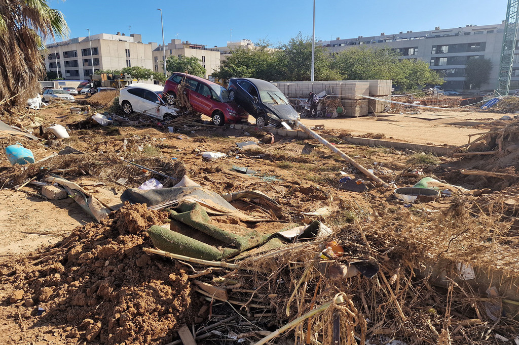 Imágenes posteriores a las inundaciones repentinas en Paiporta, Valencia, España, en noviembre de 2024, que muestran barro, escombros y tres coches dañados (uno blanco, uno rojo y uno negro) en una obra en construcción con edificios al fondo.