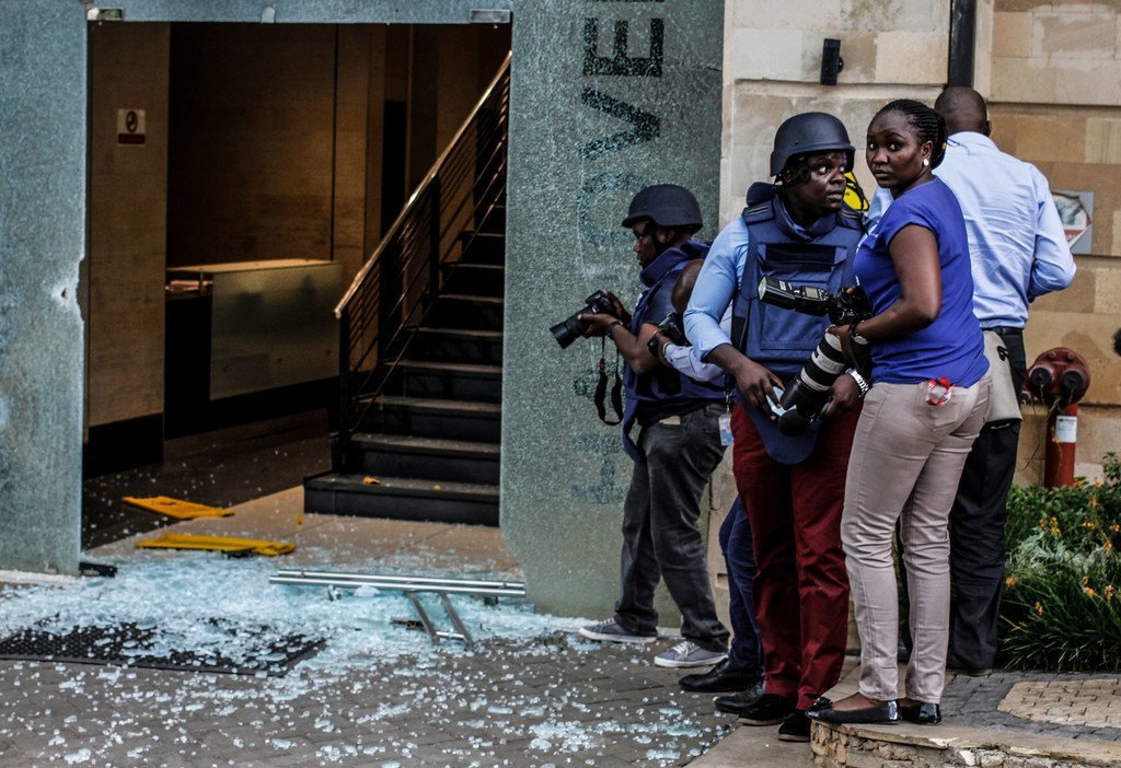 Fotógrafos con equipo de protección se encuentran cerca de los cristales rotos en la entrada del hotel Dusit D2 en Nairobi, Kenia.