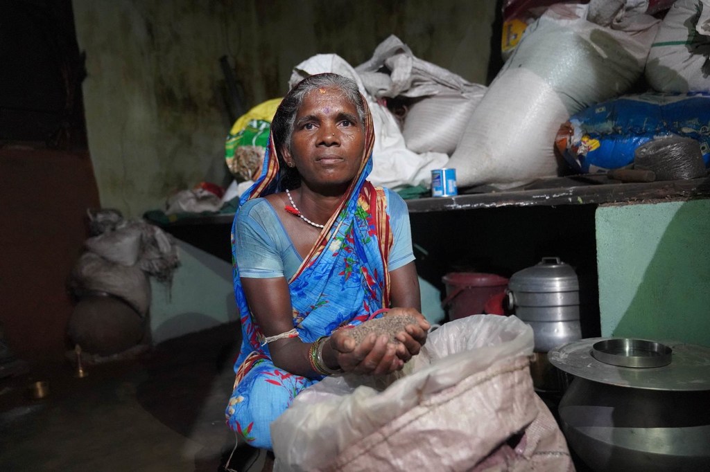 ओडिशा की बाजरा किसान पबित्रा, उपज से भरी बोरियों वाले कमरे में अपनी कटी हुई फसल के कुछ दाने पकड़े हुए है।