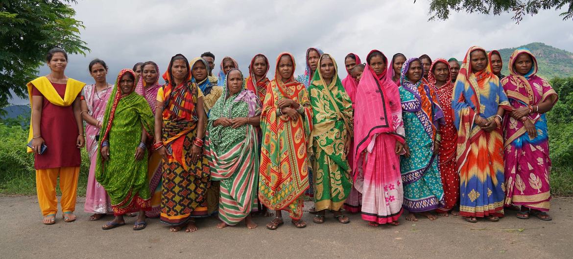 ओडिशा के ग्रामीण इलाके में रंग-बिरंगी पारंपरिक साड़ियों में सजी भारतीय महिलाओं का एक समूह खेत में खड़ा है।