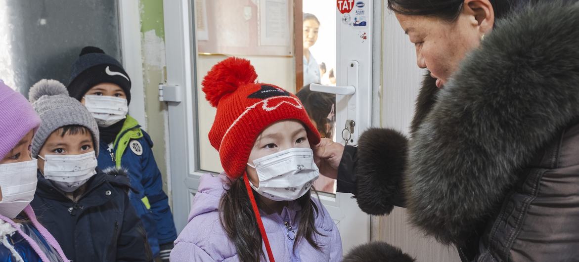 © UNICEF/Vlad Sokhin A kindergarten teacher helps a child with a face mask before outdoor activities in Nalaikh, Mongolia.