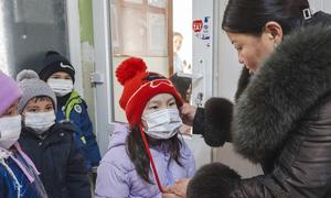 A kindergarten teacher helps a child with a face mask before outdoor activities in Nalaikh, Mongolia.