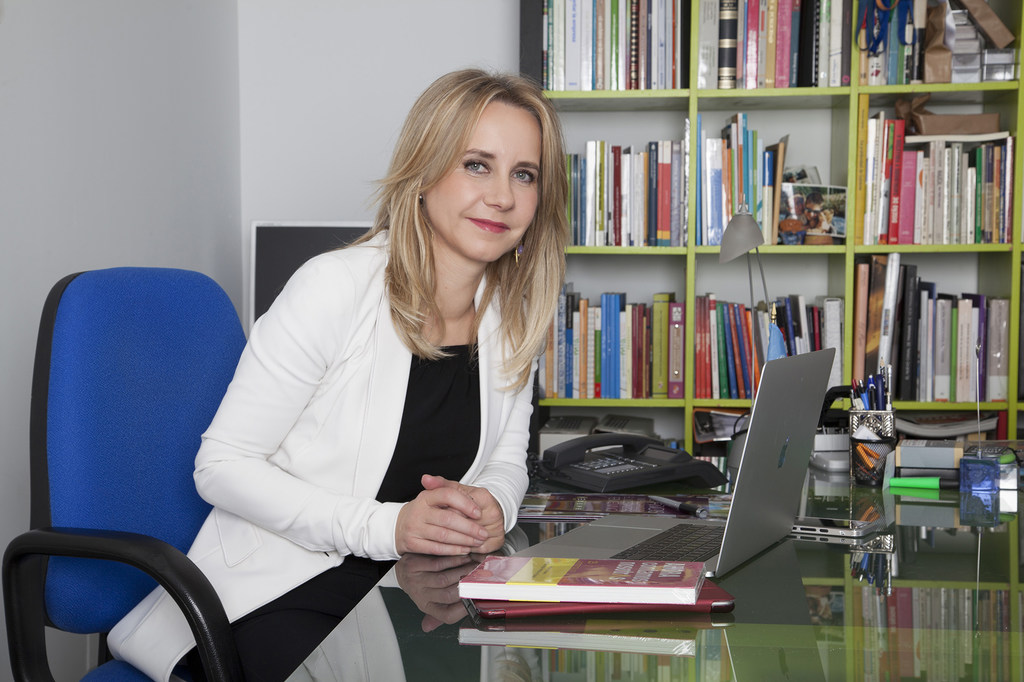 En la fotografía, Ana Bujaldón, presidenta de FEDEPE, aparece en su despacho, sentada en un escritorio con un ordenador portátil y libros.